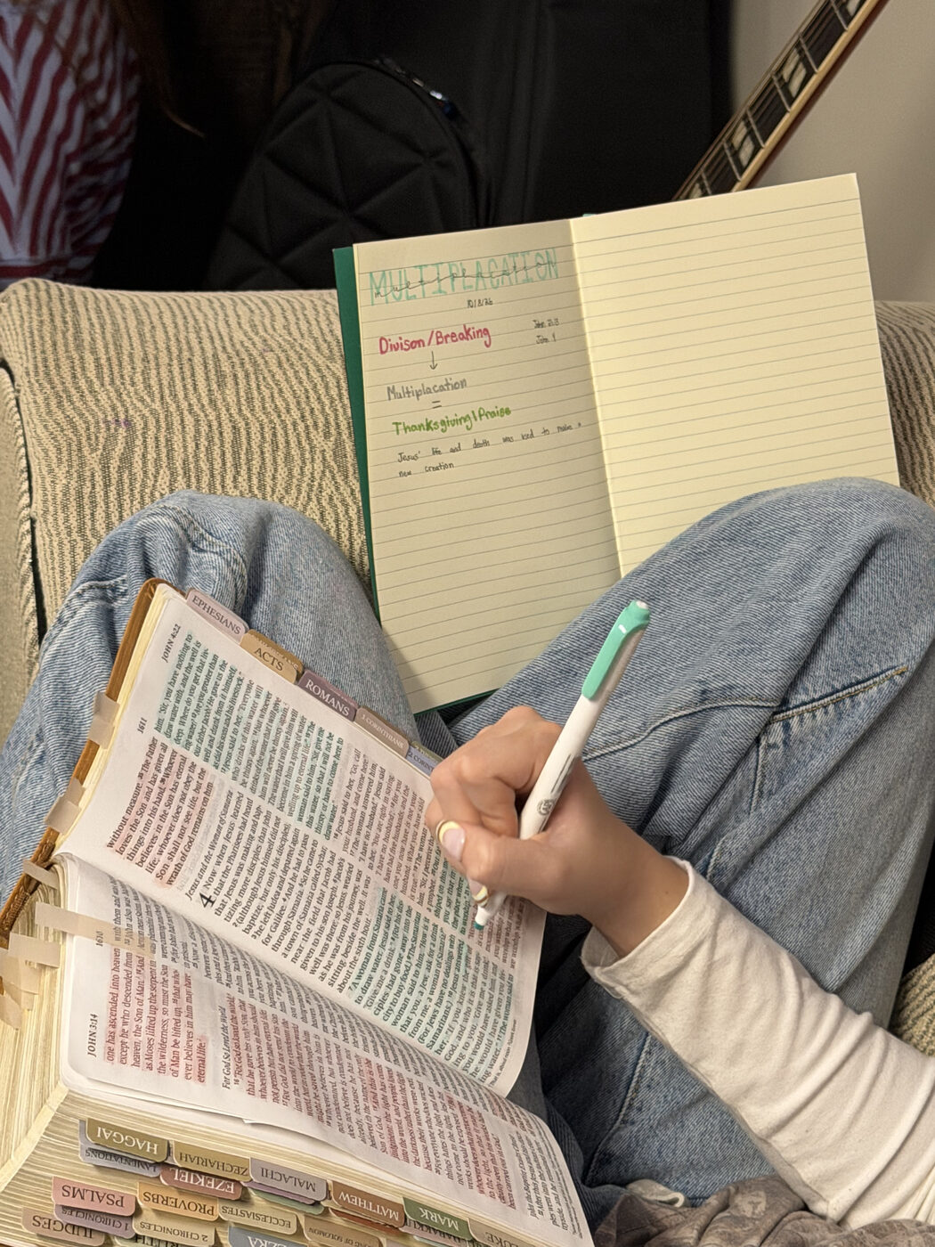 An open, tabbed Bible on a lap beside a notebook of handwritten study notes