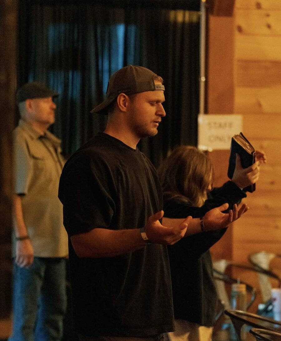 A man in a backwards cap prays with eyes closed and palms open