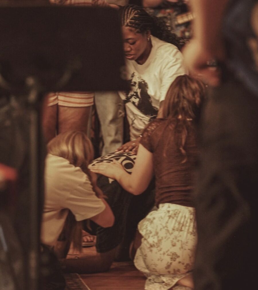 Friends kneel on the floor and lay hands on someone as they pray together