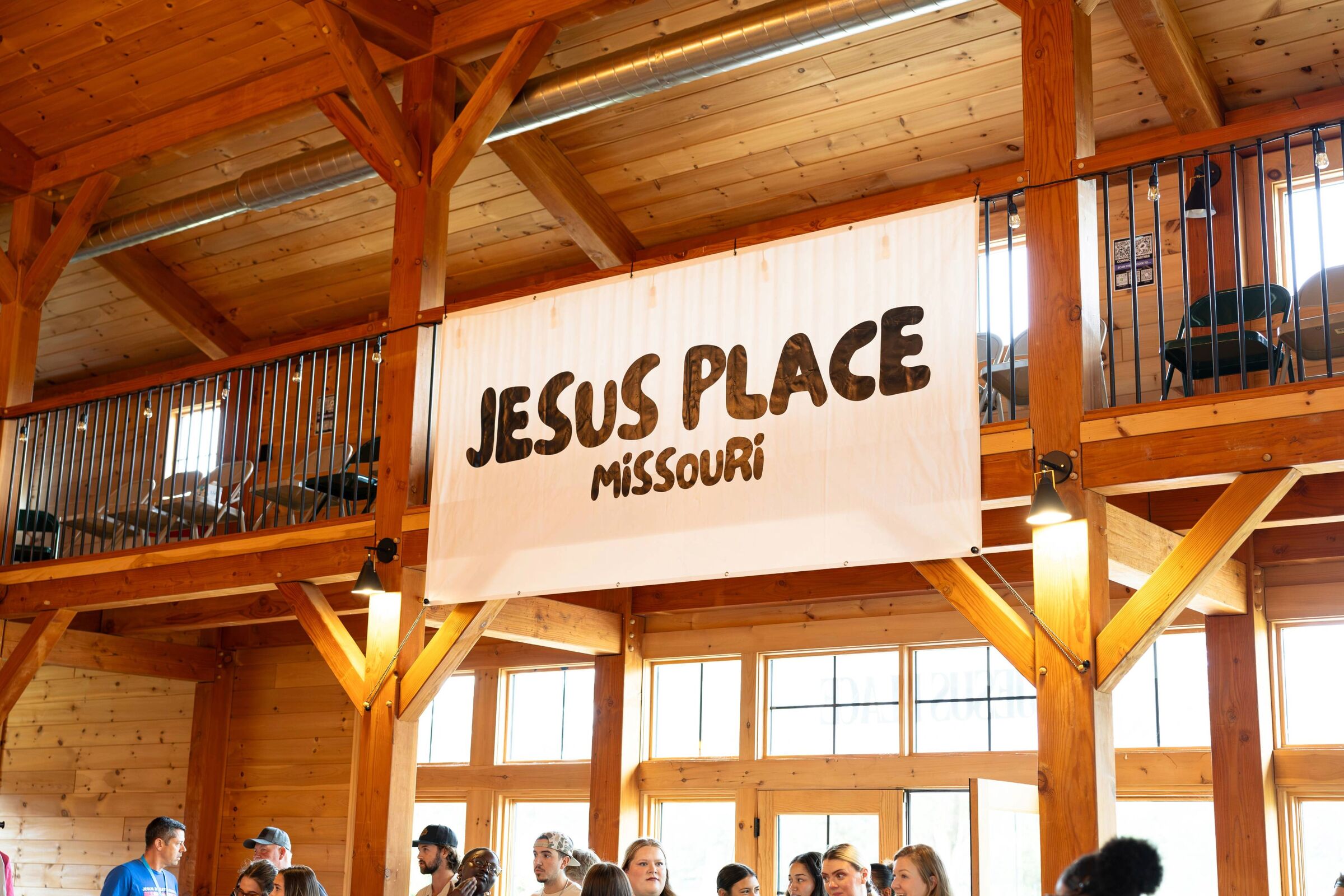 The Jesus Place Missouri banner hanging in a timber-framed barn above the gathered community