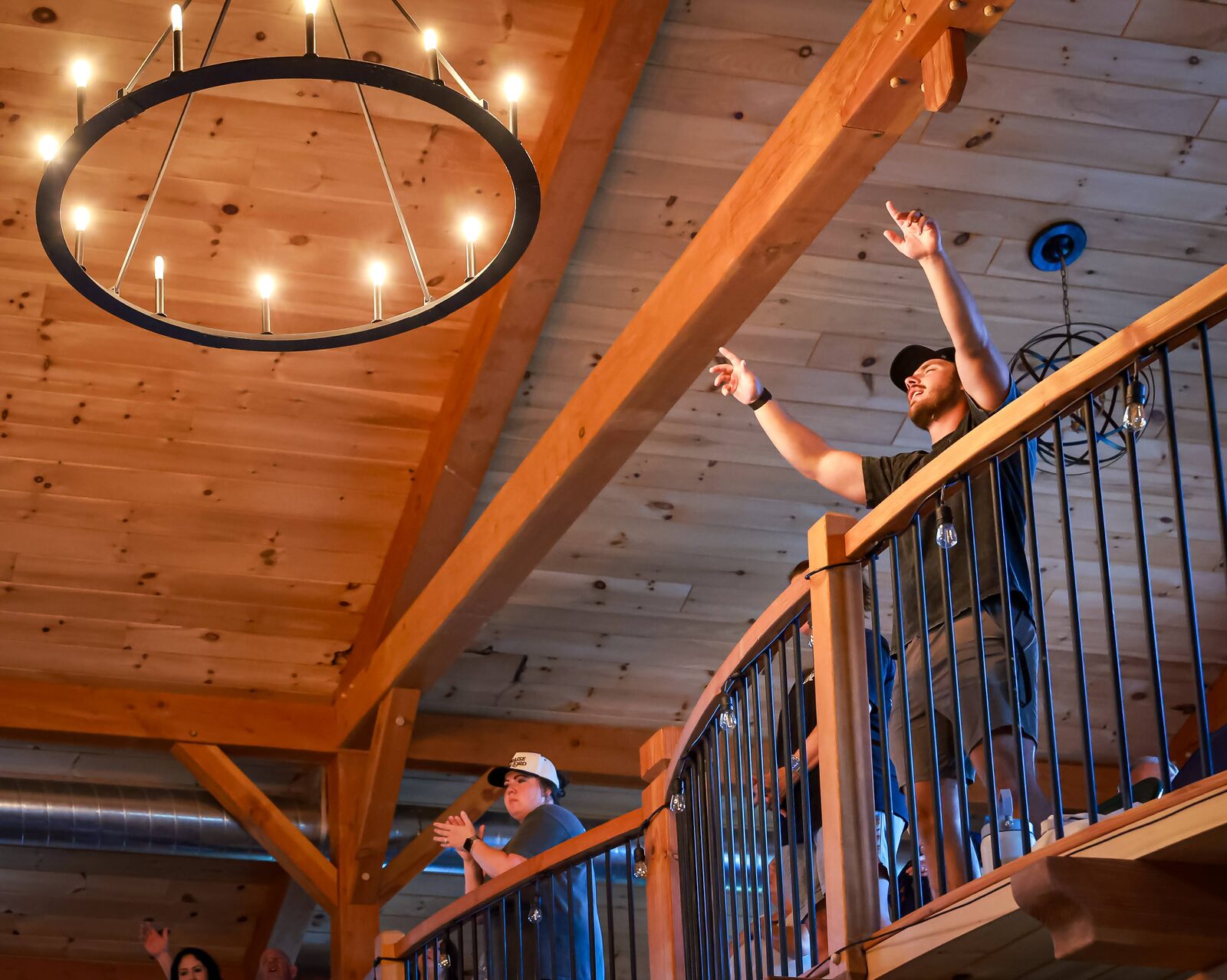 A young man on the lodge balcony with both hands lifted in praise beneath a chandelier