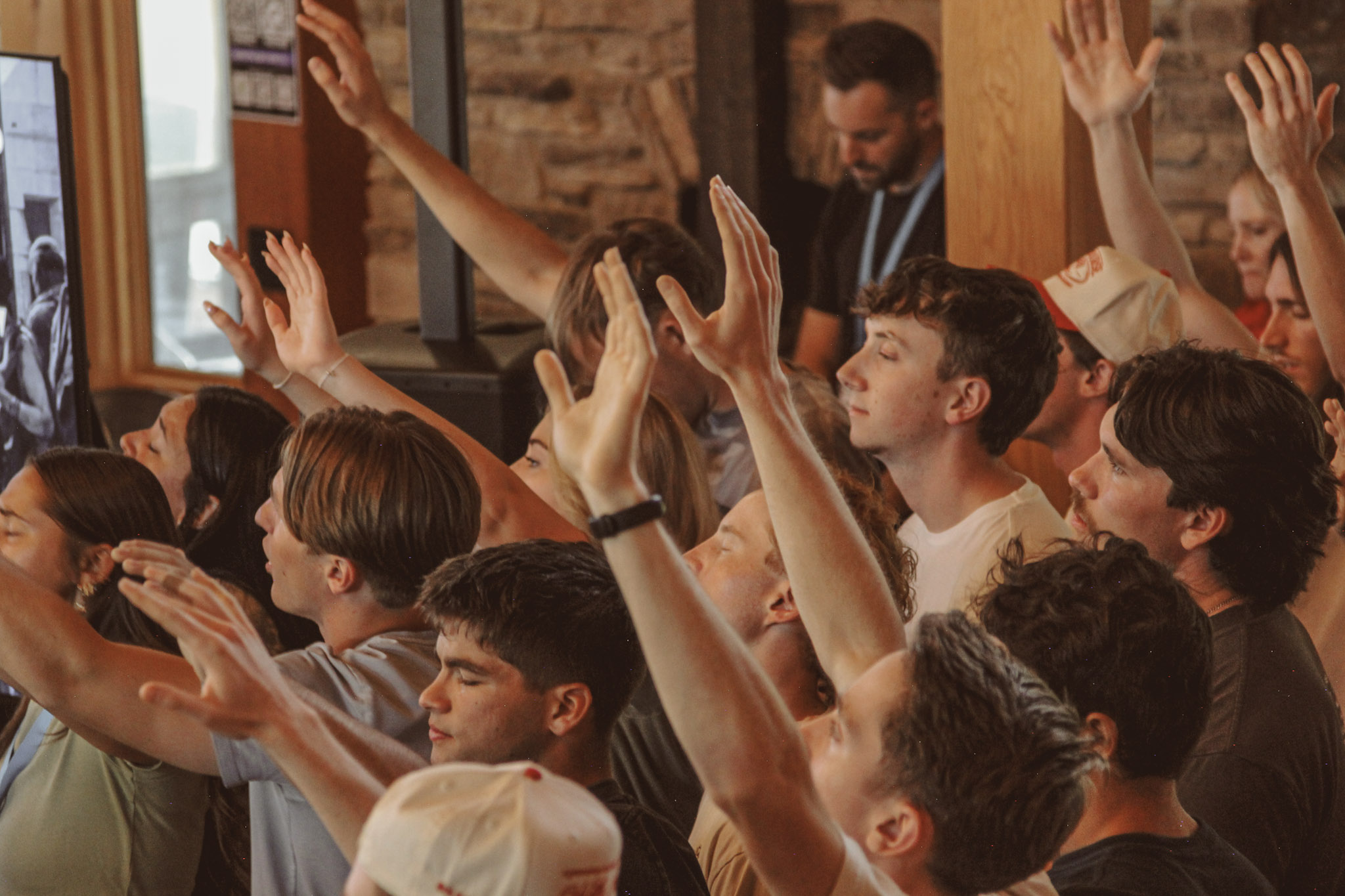A crowd of young adults worshiping with eyes closed and hands lifted high