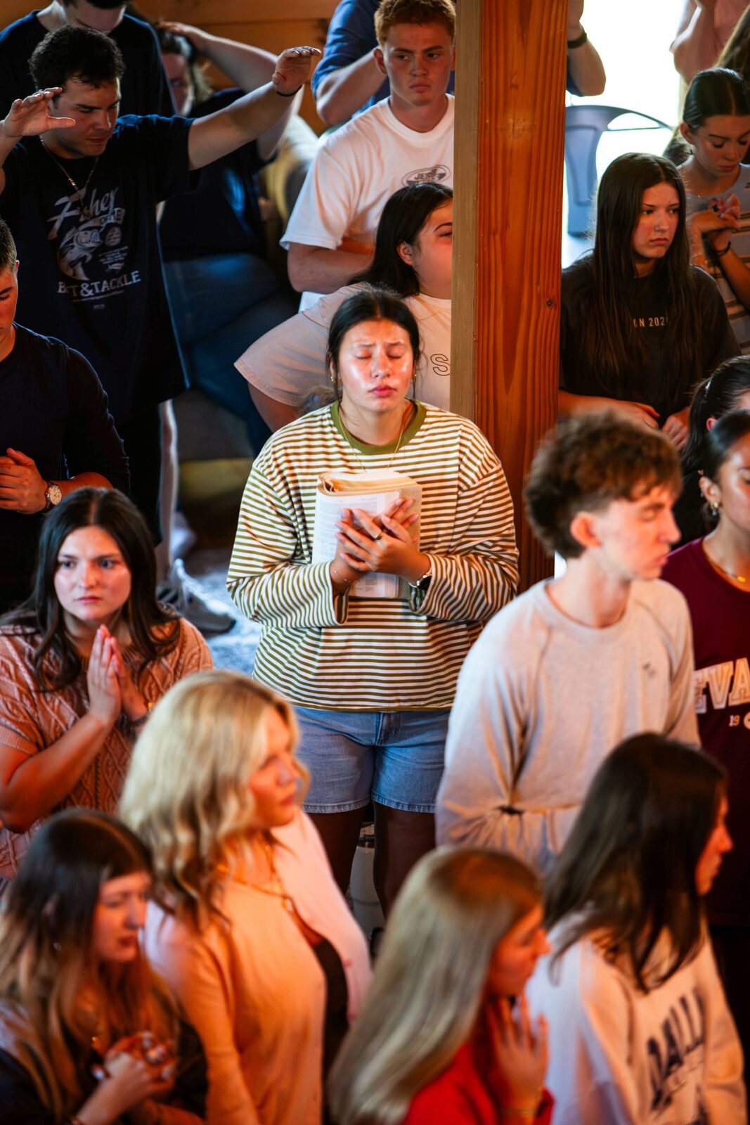 A young woman holding a Bible to her chest with eyes closed as others pray around her