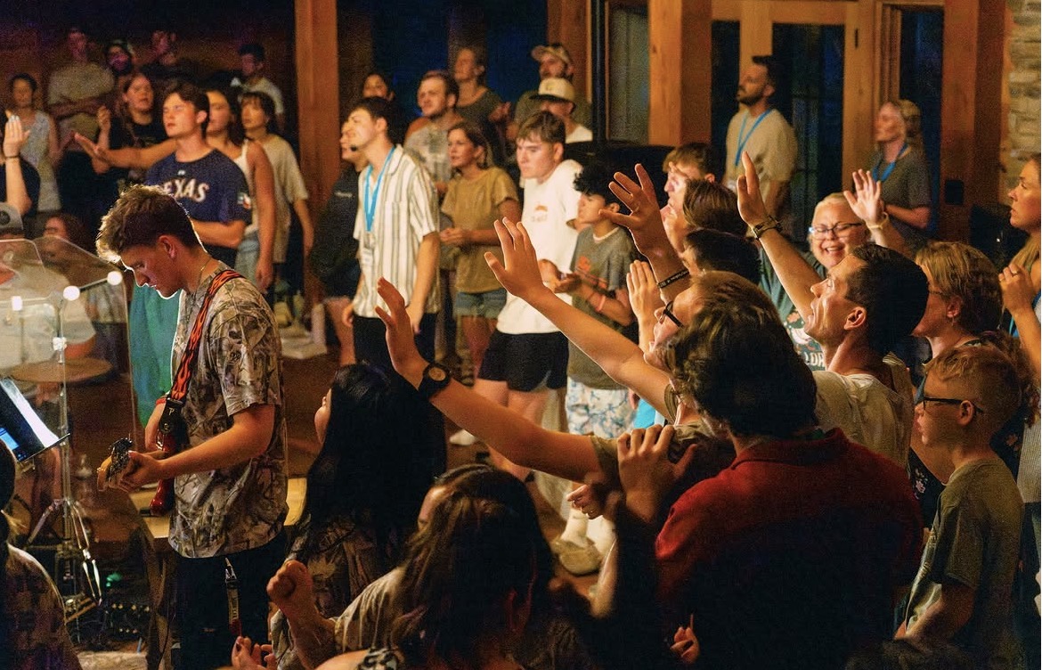 A guitarist leading worship as the gathered community raises their hands