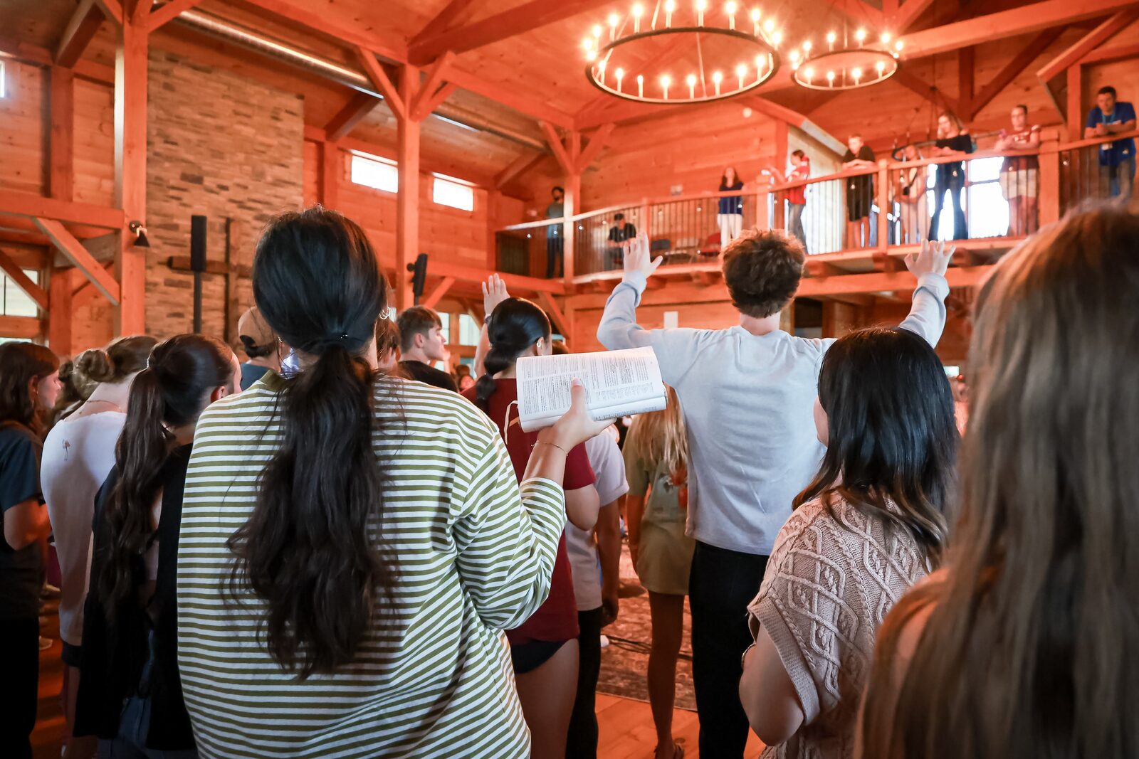 The gathered community worshiping with hands raised as one person holds an open Bible
