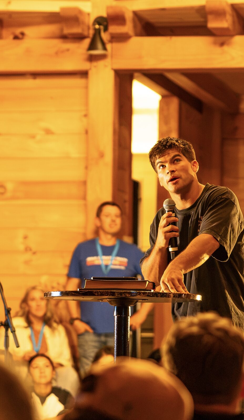 A young man leaning on a podium with a microphone, sharing a message with the gathering